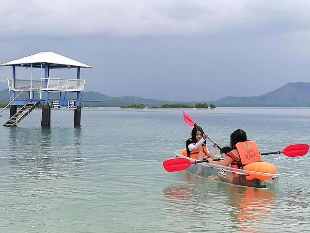 Two people kayaking in a clear kayak near a structure on stilts