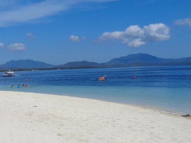 Menschen beim Schwimmen und Kajakfahren in klarem blauem Wasser nahe einem weißen Sandstrand