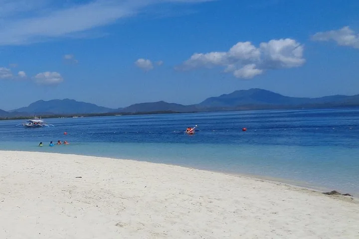 People kayaking and swimming in the ocean with mountains in the background